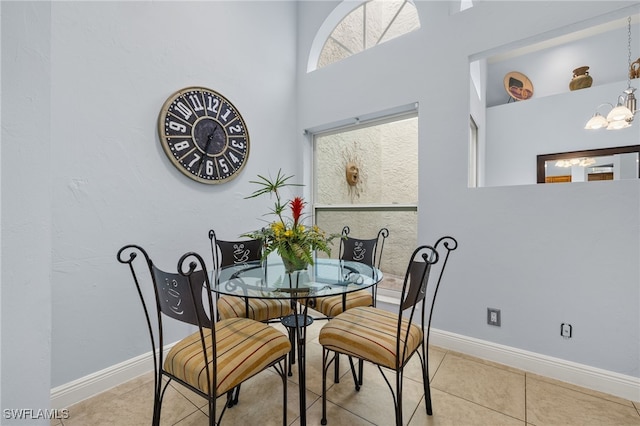 tiled dining area featuring a towering ceiling, baseboards, and a chandelier