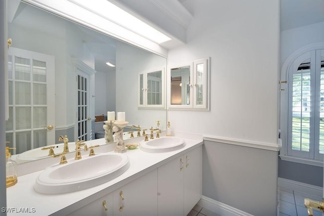 full bathroom featuring baseboards, double vanity, a sink, and tile patterned floors