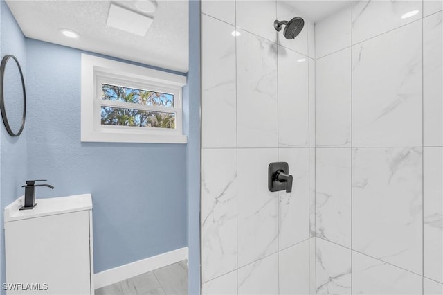 bathroom with a textured wall, a tile shower, a textured ceiling, vanity, and baseboards