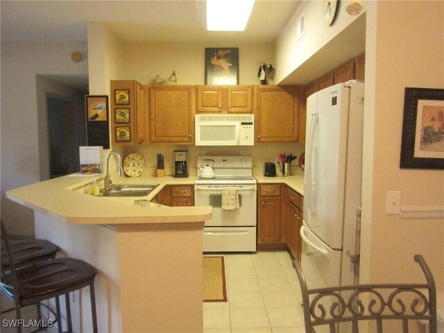 kitchen with white appliances, brown cabinetry, a peninsula, light countertops, and a sink