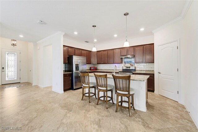 kitchen with under cabinet range hood, a kitchen breakfast bar, appliances with stainless steel finishes, decorative backsplash, and an island with sink