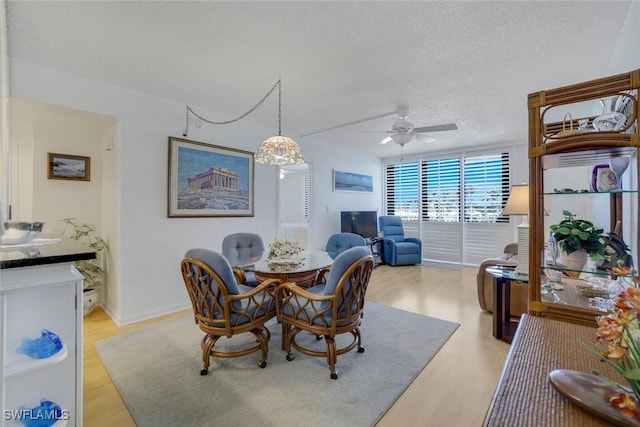 dining area featuring light wood-type flooring, ceiling fan, a textured ceiling, and baseboards