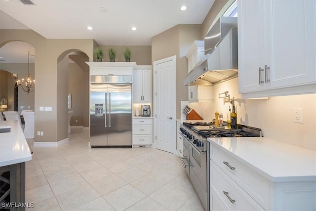 kitchen with arched walkways, white cabinetry, wall chimney range hood, high quality appliances, and a chandelier