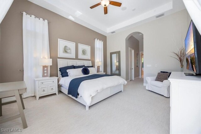 bedroom with visible vents, arched walkways, ceiling fan, light carpet, and a raised ceiling