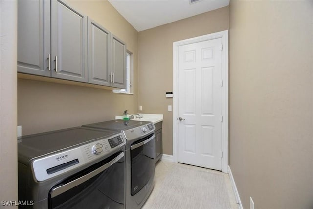 washroom with washing machine and dryer, cabinet space, baseboards, and a sink