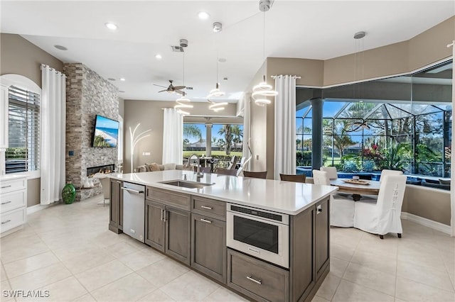 kitchen featuring a sink, open floor plan, a stone fireplace, light countertops, and ceiling fan