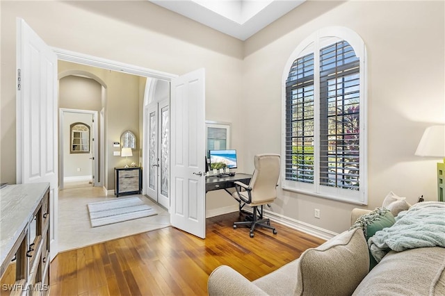 home office with hardwood / wood-style flooring, baseboards, arched walkways, and a towering ceiling