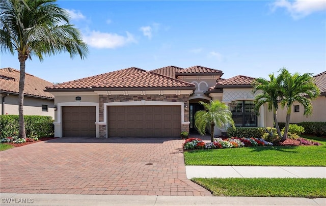 mediterranean / spanish-style home with decorative driveway, a tile roof, stucco siding, a garage, and stone siding