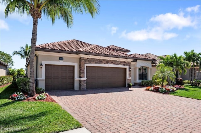 mediterranean / spanish home with stone siding, a tiled roof, an attached garage, decorative driveway, and stucco siding