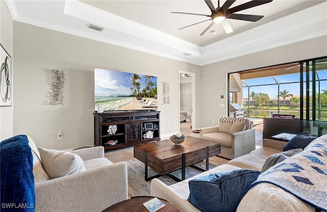 living area with a raised ceiling, ornamental molding, a ceiling fan, a sunroom, and baseboards