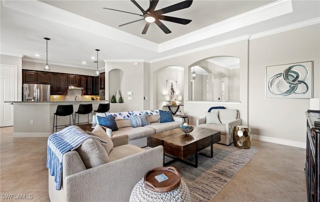 living room featuring baseboards, a raised ceiling, a ceiling fan, crown molding, and light tile patterned flooring