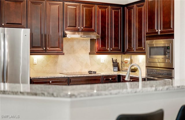 kitchen with light stone counters, stainless steel appliances, a sink, dark brown cabinets, and under cabinet range hood