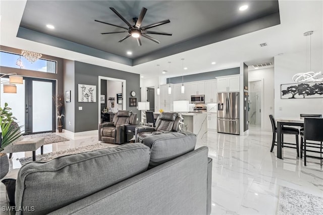 living area featuring a tray ceiling, marble finish floor, visible vents, and ceiling fan with notable chandelier