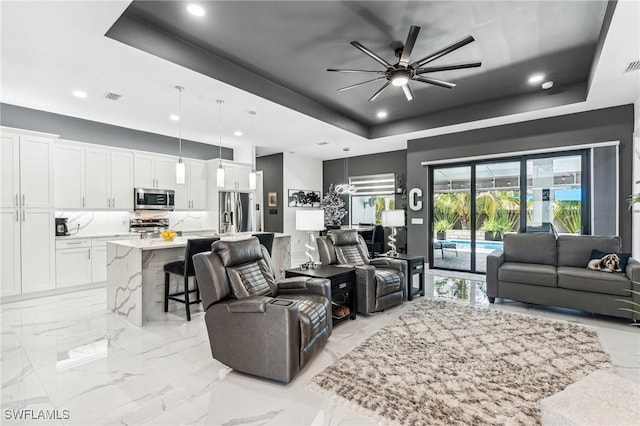 living area with recessed lighting, visible vents, a ceiling fan, marble finish floor, and a tray ceiling