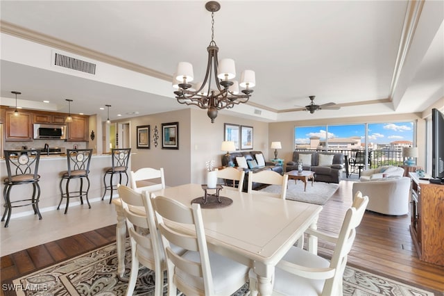 dining space featuring a tray ceiling, dark wood-type flooring, visible vents, and ornamental molding