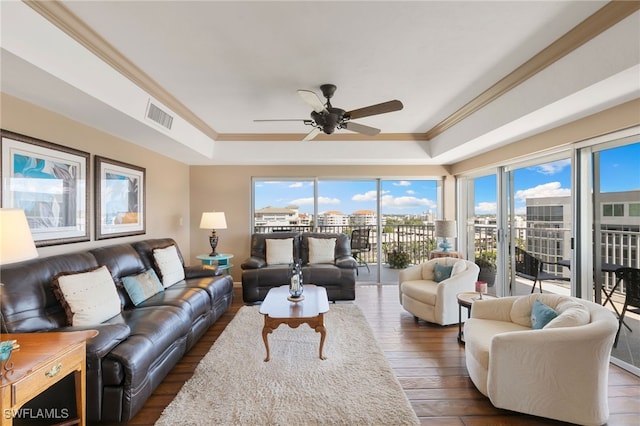 living room with visible vents, ceiling fan, a city view, a tray ceiling, and ornamental molding