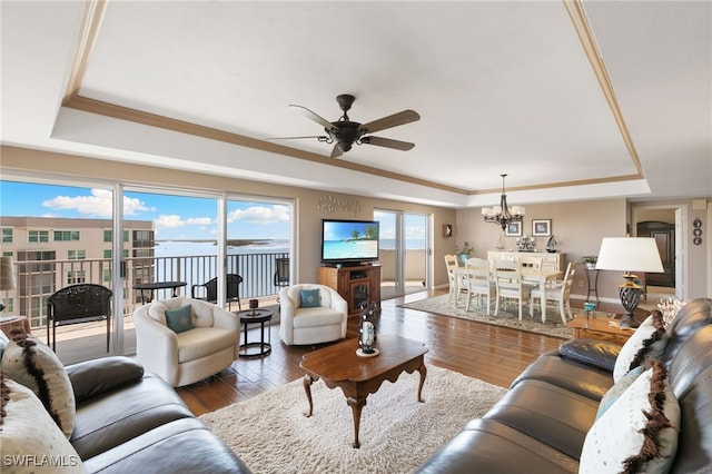 living room with ceiling fan with notable chandelier, a raised ceiling, crown molding, and wood finished floors