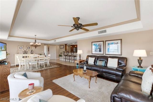 living area with visible vents, ceiling fan with notable chandelier, a raised ceiling, and wood finished floors