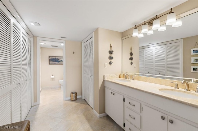 bathroom with a closet, double vanity, toilet, and a sink