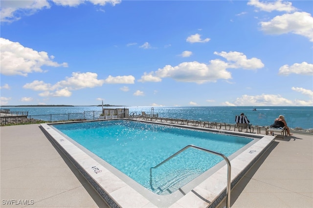 community pool featuring a patio, fence, and a water view