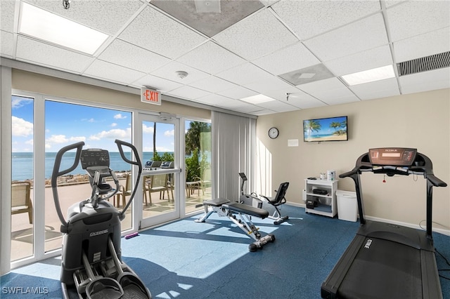 gym with a paneled ceiling, visible vents, a water view, and baseboards