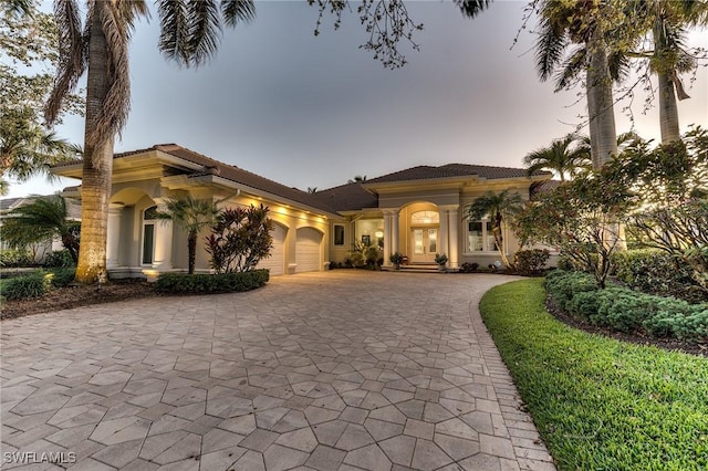 mediterranean / spanish home featuring decorative driveway, an attached garage, and stucco siding