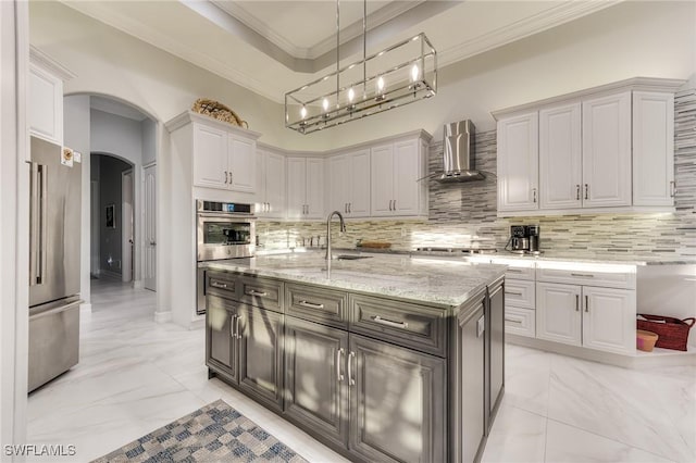 kitchen featuring arched walkways, wall chimney exhaust hood, appliances with stainless steel finishes, marble finish floor, and a sink