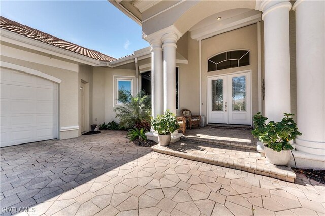 view of exterior entry with a tiled roof, french doors, an attached garage, and stucco siding