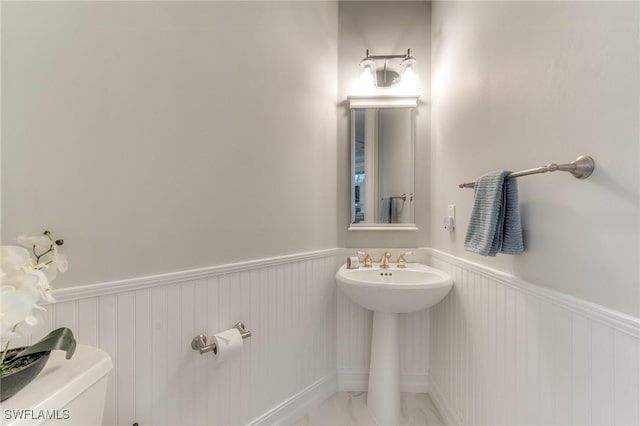 bathroom with toilet, a wainscoted wall, and a sink