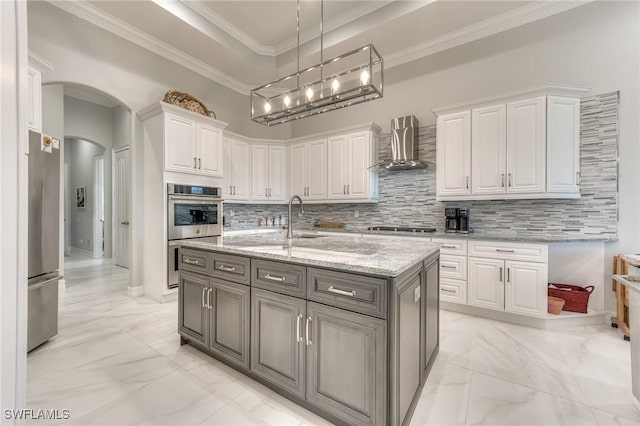 kitchen featuring arched walkways, white cabinets, marble finish floor, wall chimney range hood, and a tray ceiling