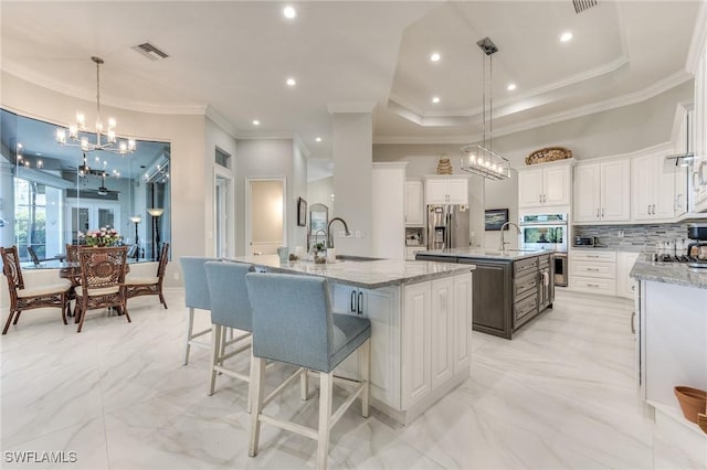 kitchen featuring stainless steel appliances, a large island with sink, backsplash, and a sink