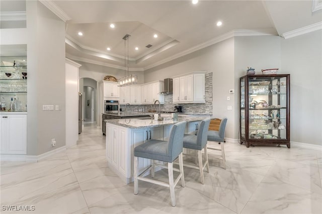 kitchen with arched walkways, oven, marble finish floor, wall chimney exhaust hood, and an island with sink