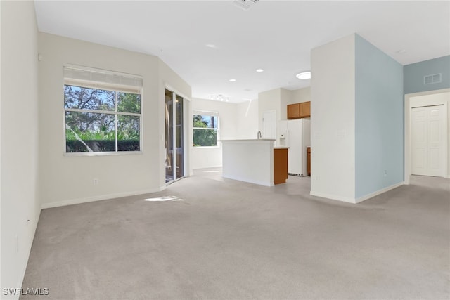 unfurnished living room featuring baseboards, visible vents, and light carpet