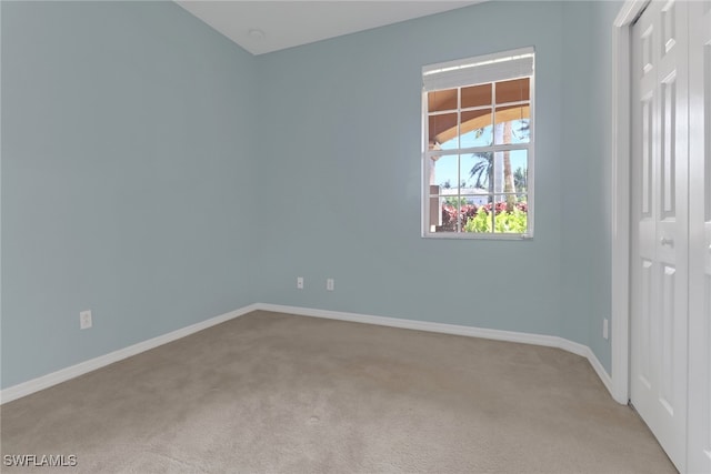 spare room featuring light colored carpet and baseboards