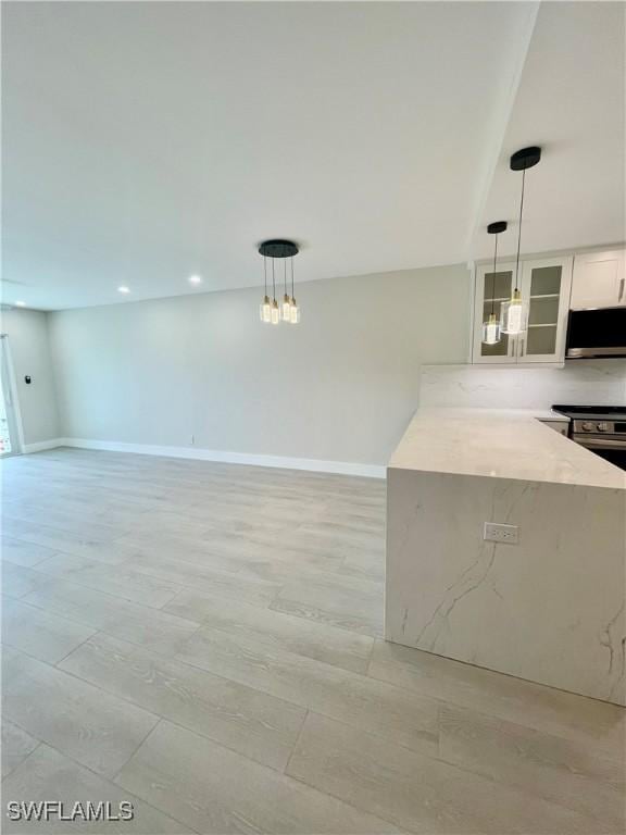 kitchen featuring glass insert cabinets, pendant lighting, stainless steel microwave, and white cabinets