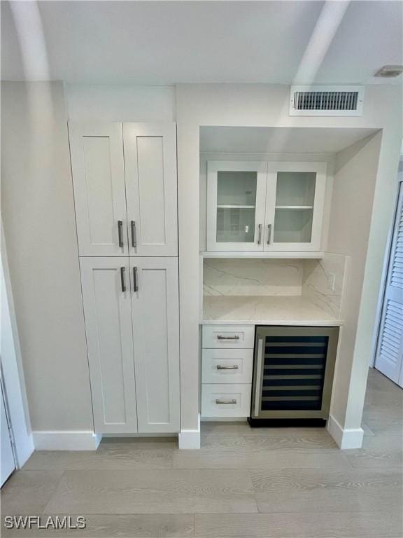 bar with wine cooler, a dry bar, visible vents, baseboards, and light wood finished floors