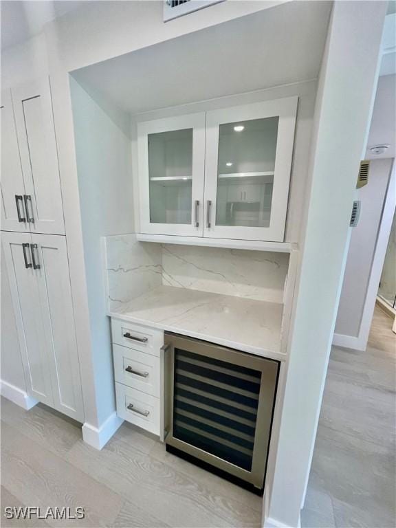 bar with light wood finished floors, wine cooler, baseboards, and tasteful backsplash