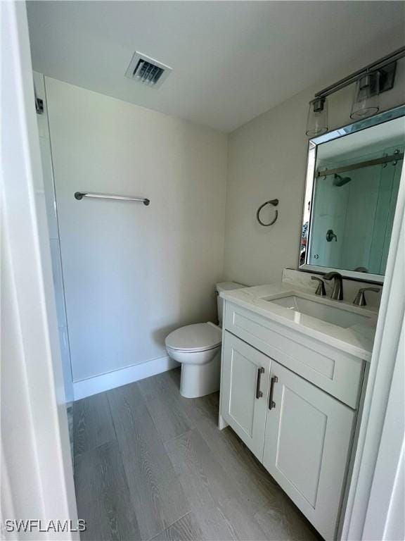 full bathroom with visible vents, a shower, toilet, wood finished floors, and vanity