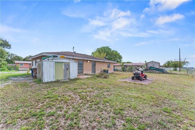 rear view of house with a storage shed, a lawn, an outbuilding, fence, and stucco siding