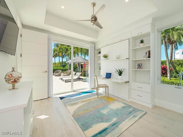 living area featuring a ceiling fan, baseboards, a tray ceiling, recessed lighting, and light wood-style floors