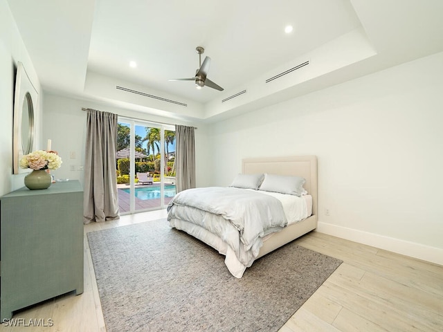 bedroom featuring access to exterior, a raised ceiling, baseboards, and wood finished floors