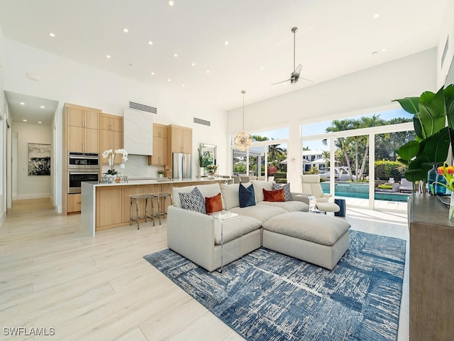 living room with a ceiling fan, visible vents, recessed lighting, light wood-style floors, and a towering ceiling