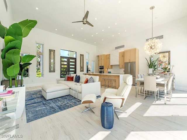 living area with visible vents, light wood-style flooring, recessed lighting, ceiling fan with notable chandelier, and a high ceiling