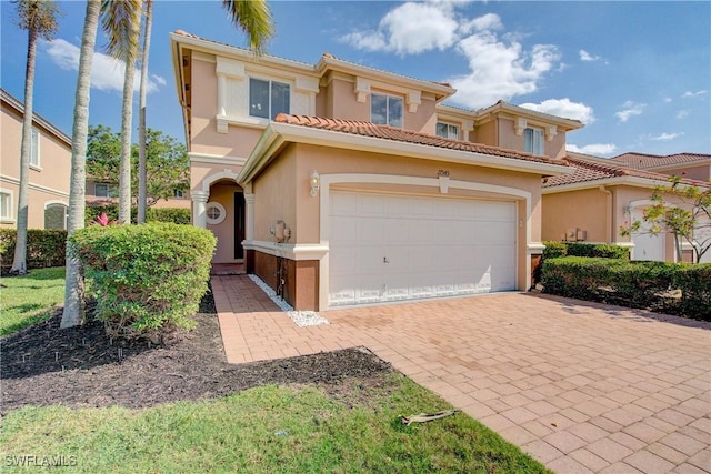 mediterranean / spanish home with a garage, a tiled roof, decorative driveway, and stucco siding