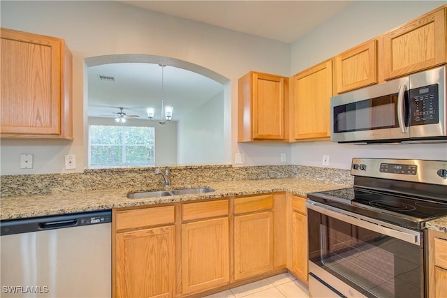 kitchen with light stone counters, arched walkways, light tile patterned floors, appliances with stainless steel finishes, and a sink