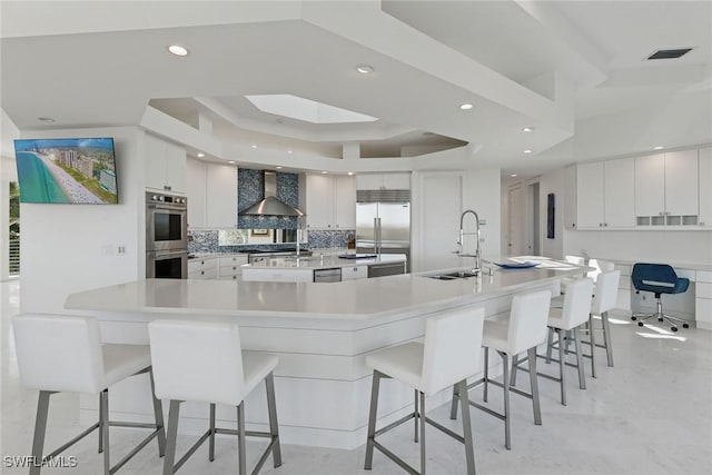 kitchen featuring visible vents, a sink, appliances with stainless steel finishes, a breakfast bar area, and wall chimney range hood