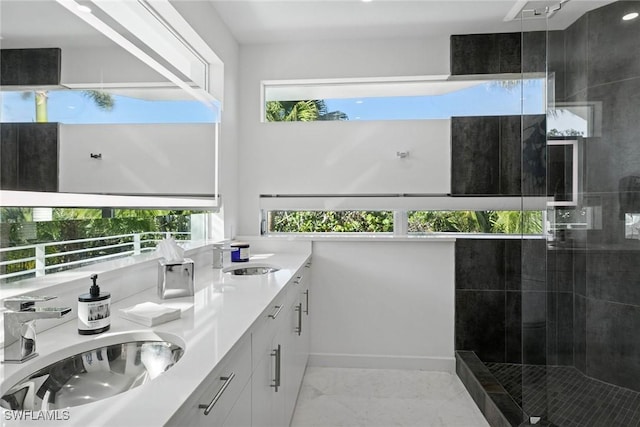 full bath with a sink, marble finish floor, double vanity, and a tile shower