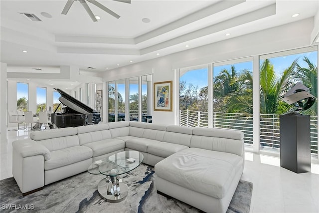 living area featuring a wealth of natural light, visible vents, ceiling fan, and a tray ceiling