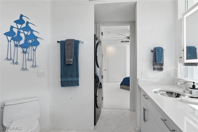 ensuite bathroom with vanity, a ceiling fan, stacked washer and dryer, toilet, and marble finish floor