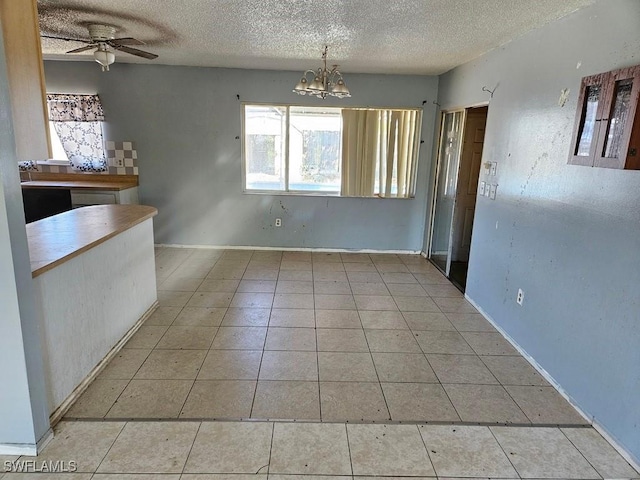 unfurnished dining area with ceiling fan with notable chandelier, a textured ceiling, and light tile patterned flooring